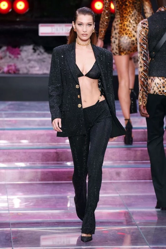 bella hadid walking down the runway, wearing black sequinned suit, consisting of pants bra and blazer, current fashion trends