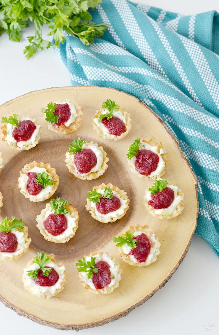 shells filled with cheese and cranberry jam, best appetizer to bring to a party, arranged on wooden board, next to blue cloth