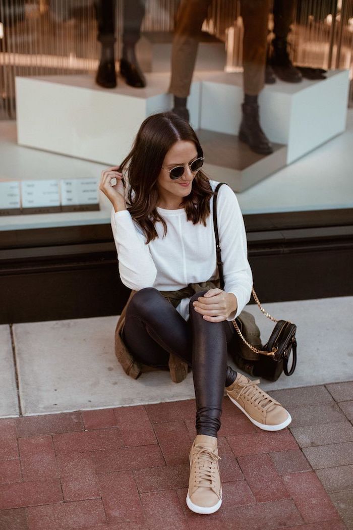 woman sitting on the street, current fashion trends, wearing black leather tights and white blouse, beige sneakers and black bag