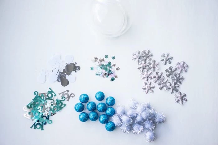 blue and silver pompoms, christmas ornament crafts, silver snowflakes, placed on white surface, step by step diy tutorial