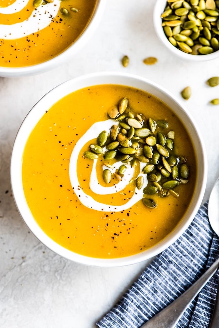 pumpkin soup, pumpkin seeds for garnish, in white ceramic bowl, chicken tortellini soup, blue table cloth