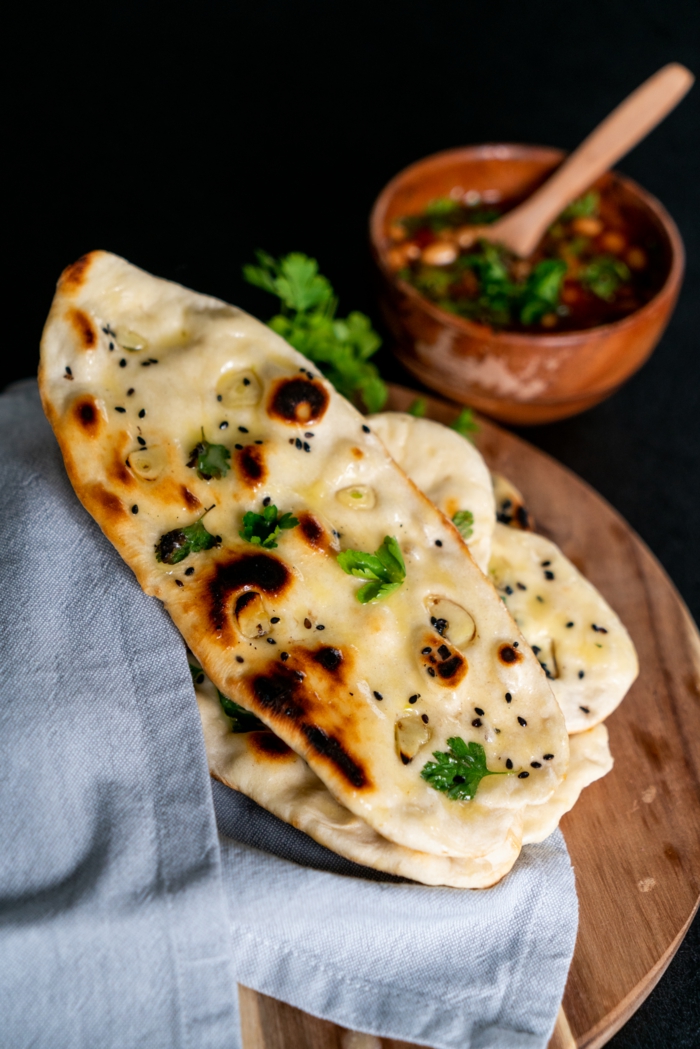 naan bread with garlic and parsley, placed on wooden cuttin board, naan bread recipe, blue coth next to it