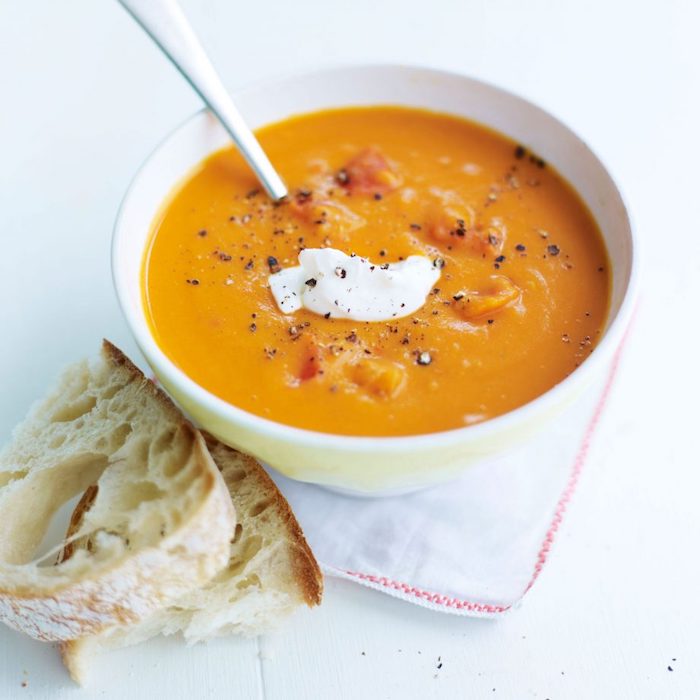 bread slice on the side, chicken tortellini soup, cream soup in a white ceramic bowl, spoon inside