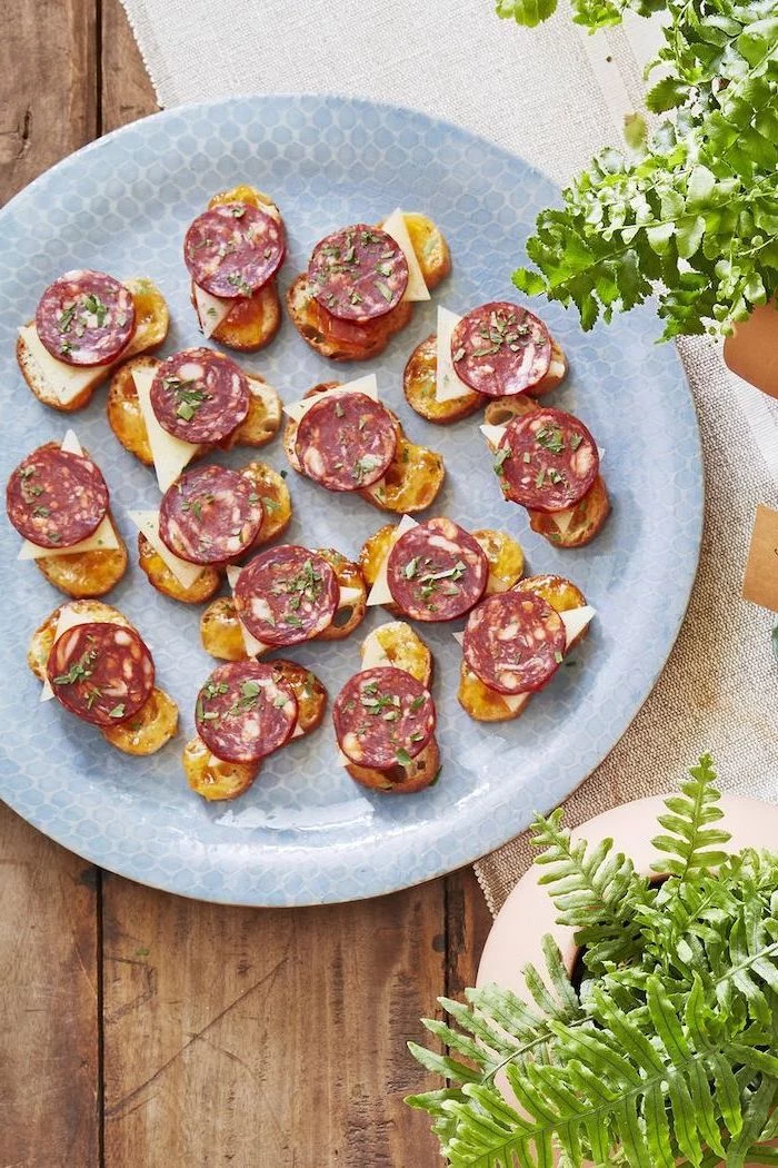 bruschetta with chorizo and cheese, arranged on blue plate, best appetizer to bring to a party, placed on wooden surface