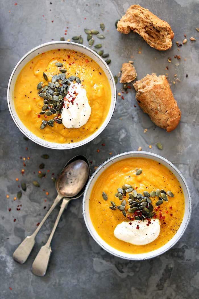 two bowls full of soup, pumpkin seeds for garnish, two spoons and bread on the side, how to make potato soup