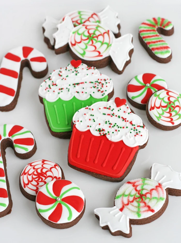 cookies in the shapes of candy canes and cupcakes, cookie decorating icing, colorful red white and green icing on top