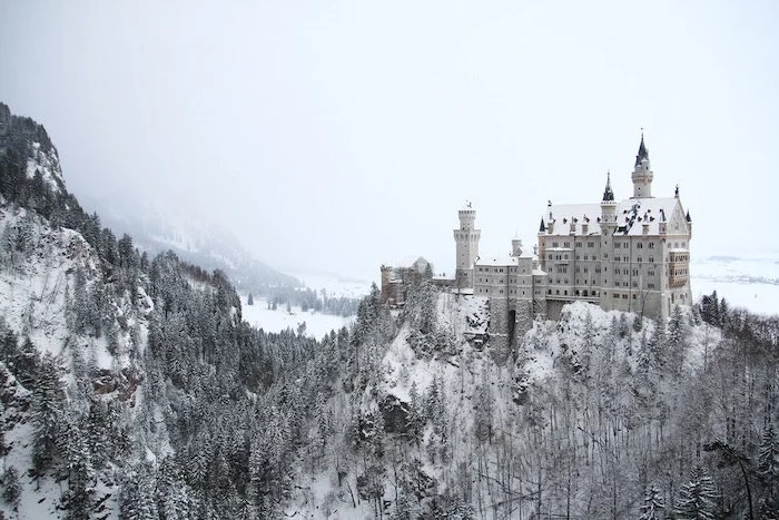 castle on a hill, surrounded by hills and tall trees, covered with snow, winter background, fog looming over it