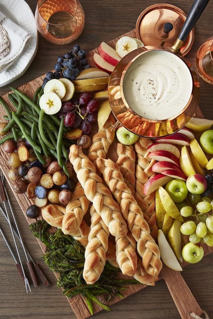 easy christmas appetizers, large wooden board, bread fruits and vegetables on it, cheese fondue in a brass bowl