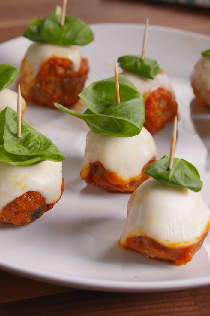 cheese mozzarella bites, basil leaves on top, easy christmas appetizers finger foods, arranged on white plate