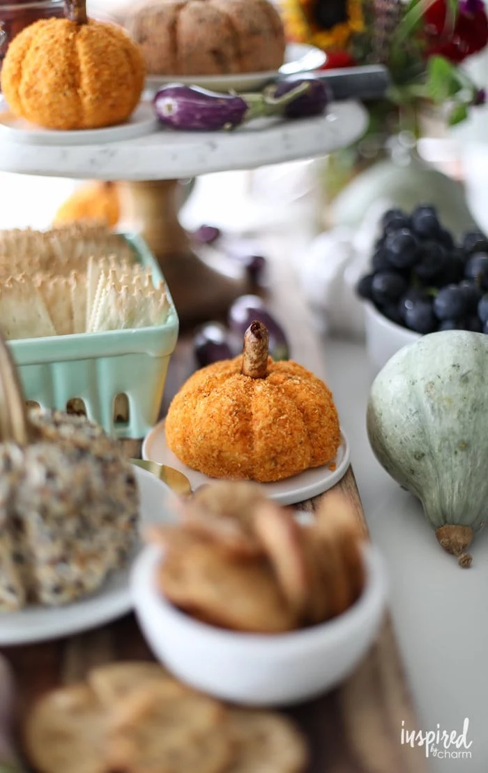cheeseballs in the shape of pumpkins, placed on white plates, easy christmas appetizers, surrounded by different bowls