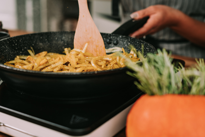 chopped onion and garlic, cumin and ginger powder, cooking in black skillet, potato soup recipe, stirred with wooden spatula