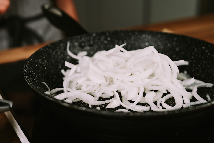 chopped onion cooking in a black skillet, placed on a hot plate, creamy soup recipes, blurred background