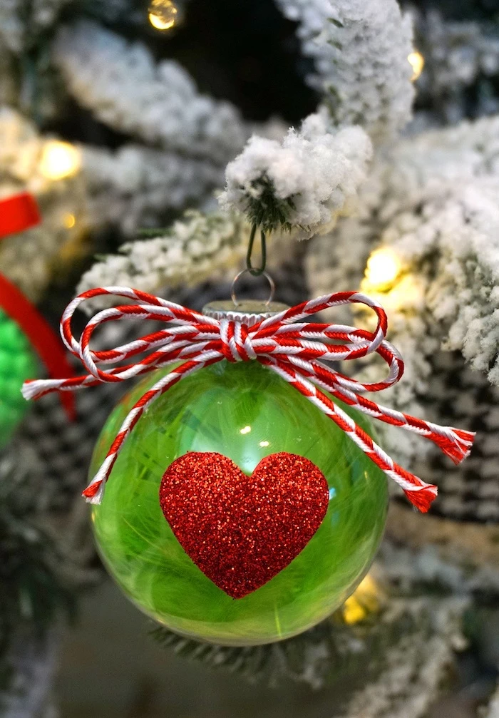 plastic bauble, filled with green feathers, easy christmas crafts for kids, red glittery heart in the front, red and white bow on top