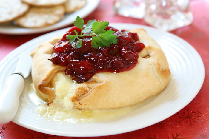 baked brie inside dough, easy christmas appetizers finger foods, cranberry jam on top, placed on white plate, knife on the side