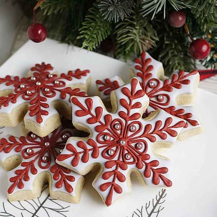 snowflake shaped cookies, with red and white icing, christmas cookie icing, placed on white plate, silver sugar pearls on top