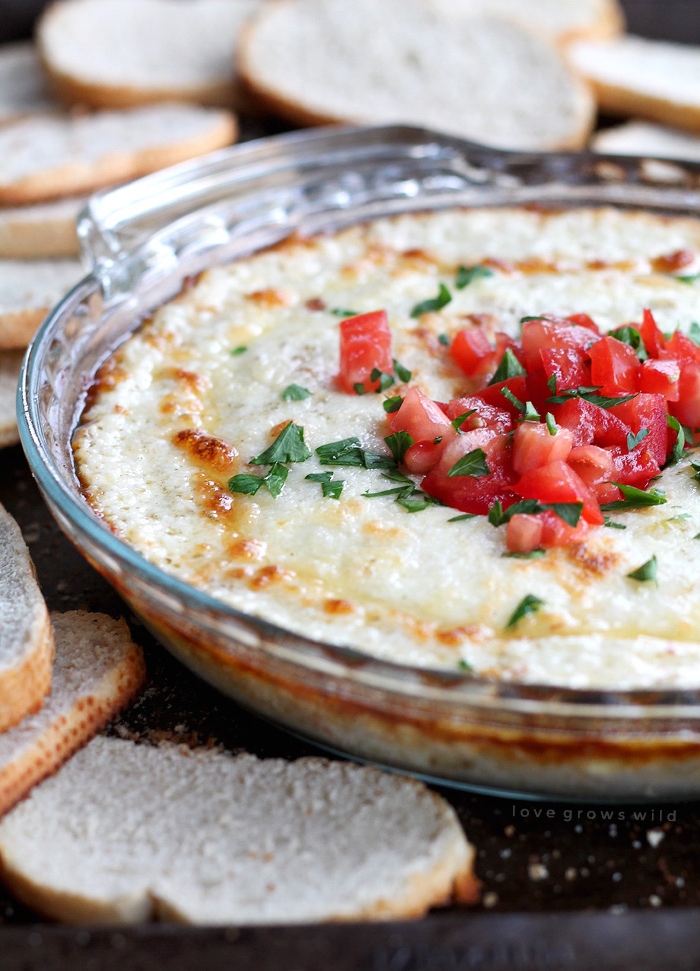 smoked mozzarella dip in glass bowl, christmas appetizers, chopped parsley and tomatoes on top, bread slices around it