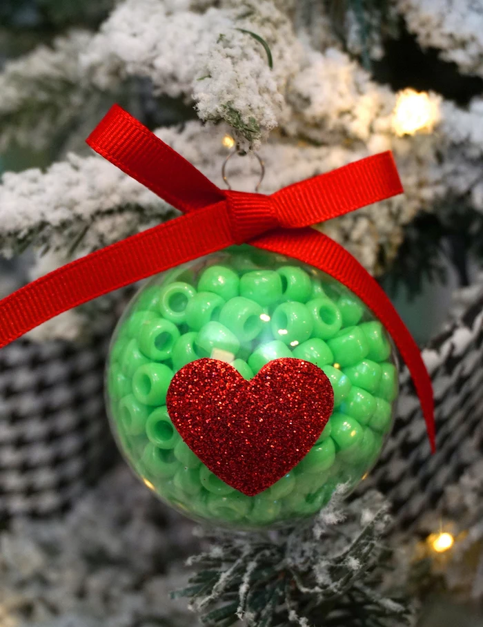 plastic bauble filled with green beads, easy christmas crafts for kids, red bow on top, glittery red heart at the front