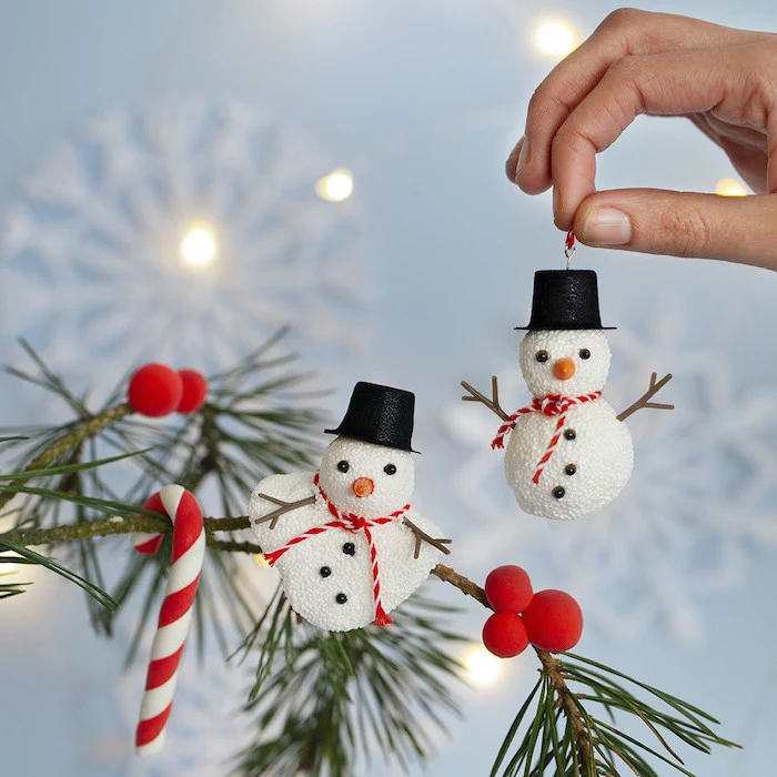two snowmen made of styrofoam balls, hanging on tree branches, easy christmas crafts for kids, red pompoms and candy cane