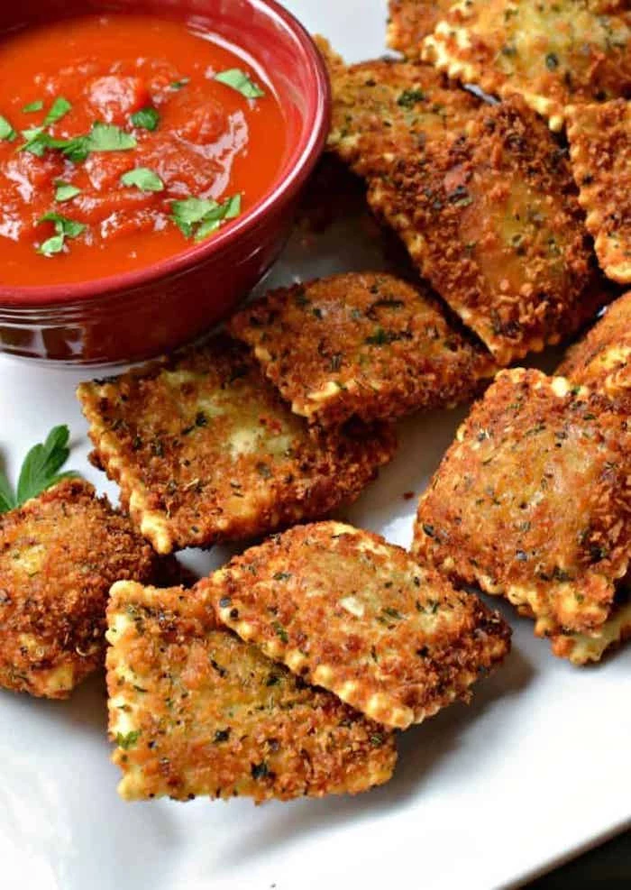 toasted ravioli, arranged on white plate, next to a ceramic bowl filled with tomato sauce, easy appetizers finger foods, parsley garnish