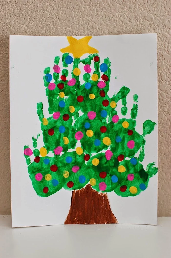 christmas tree made of handprints, painted on white paper, leaning on white wall, christmas ornaments for kids