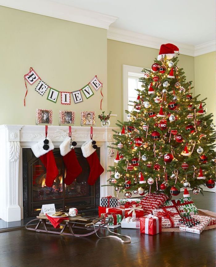 christmas tree next to the fireplace, decorated with lights and red ornaments, christmas tree ribbon, wrapped presents underneath