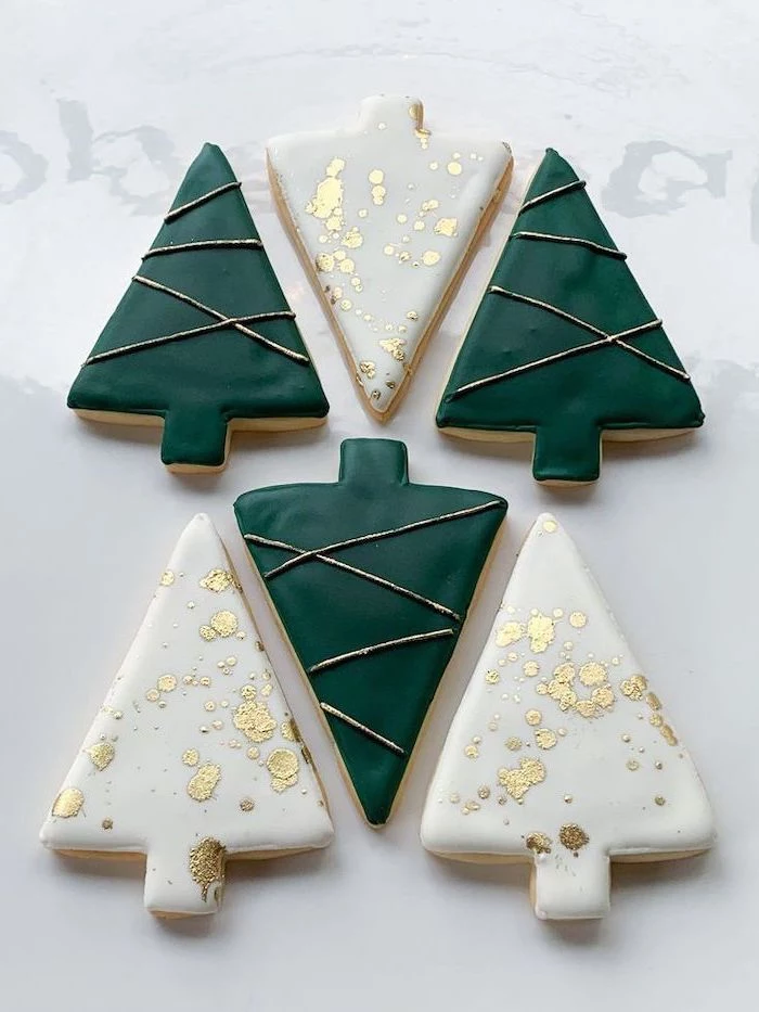 christmas tree shaped cookies, green white and gold icing on top, cookie icing, placed on white surface