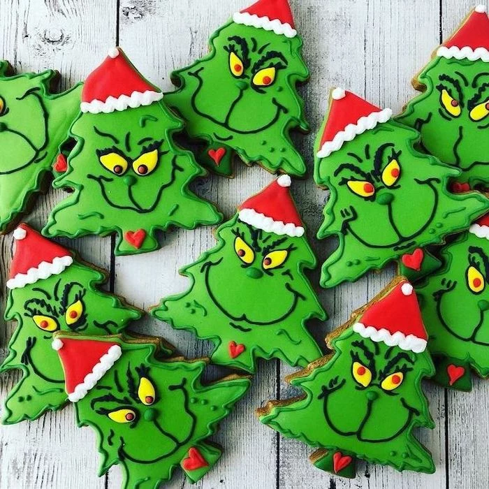 christmas tree shaped cookies, face of the grinch on them, decorated with green icing, decorated sugar cookies