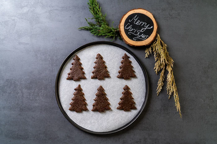 six christmas tree shaped cookies, placed on paper lined baking sheet, vegan gingerbread cookies, placed on grey surface
