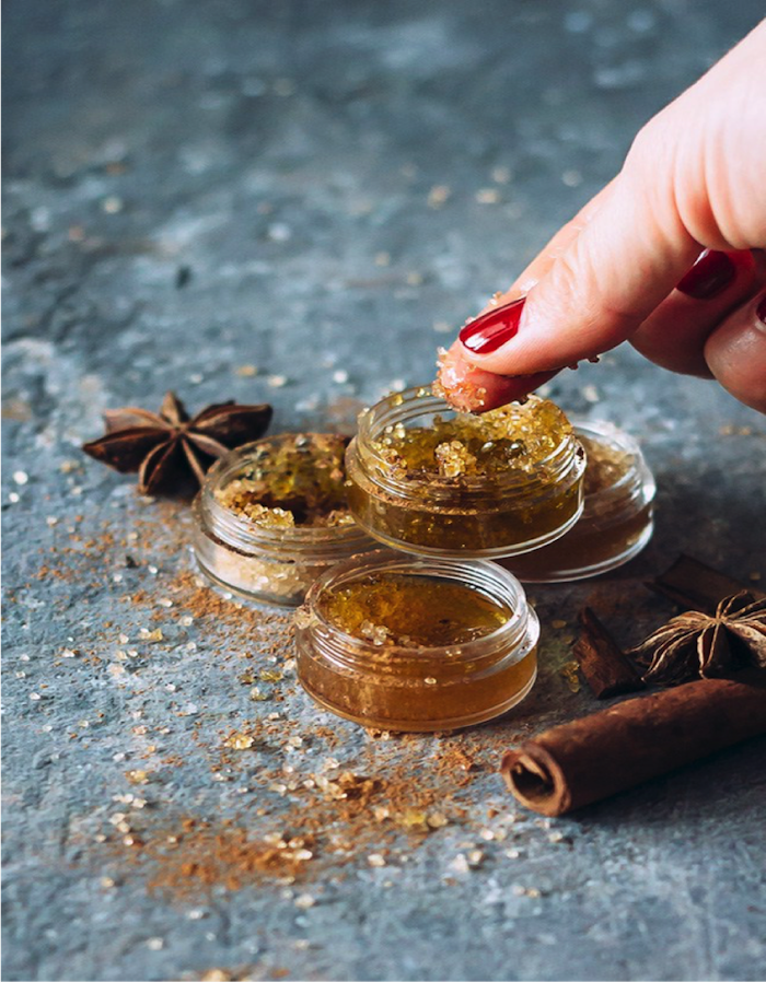 cinnamon lip scrub in a small container, best christmas gifts for mom, cinnamon sticks spread around it