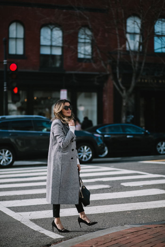 woman walking down the street, 2019 fashion trend forecast, wearing black pants and heels, long plaid coat in black and white