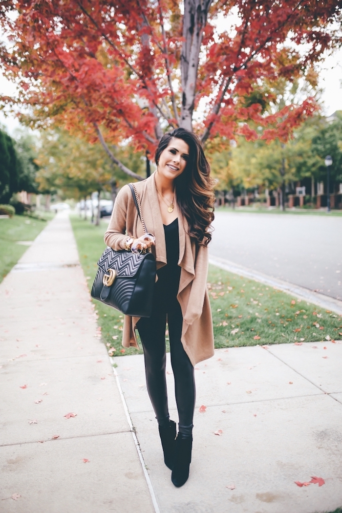 woman with long brown hair, wearing black leather tights and top, fall trends, long beige cardigan on top, black bag and velvet boots
