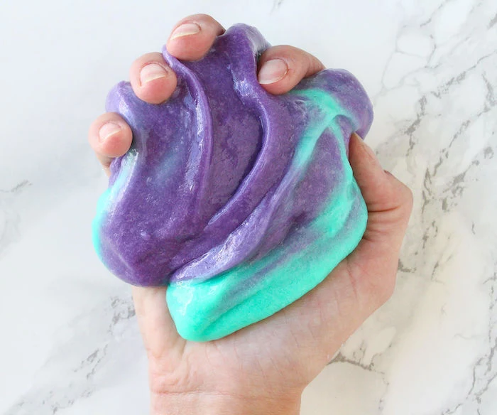 color changing slime, in turquoise and purple, held in hand, on marble countertop, how to make slime with glue