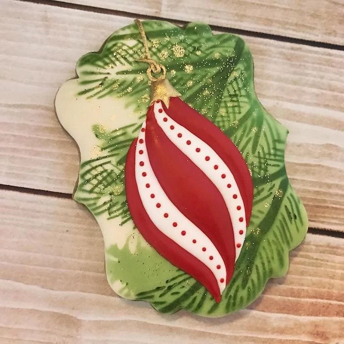 cookie painted with green and white icing, red ornament drawn on it, placed on wooden surface, cookie decorating icing