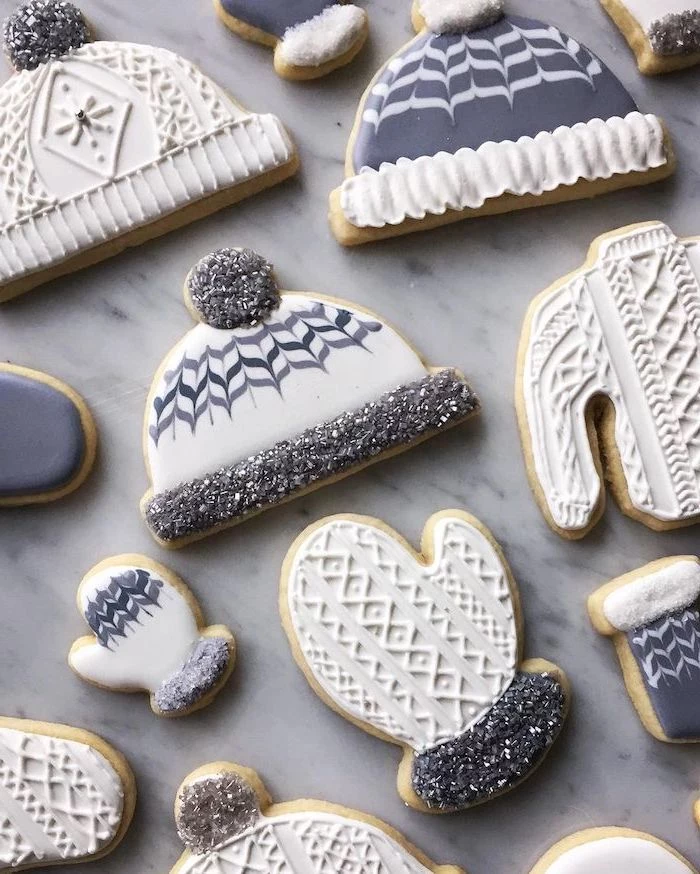 cookies in the shapes of beanies and mittens, cookie decorating icing, decorated with grey and white icing, placed on marble surface