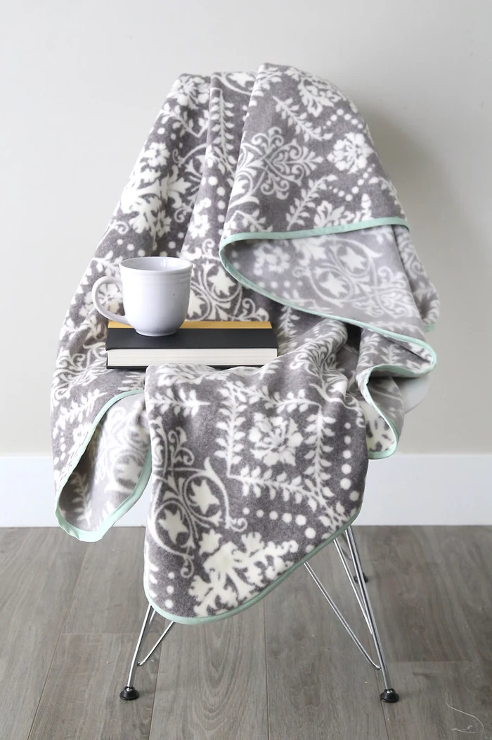 grey fleece blanket spread out on a chair, book and coffee mug on top of it, chair on wooden floor, christmas presents for moms
