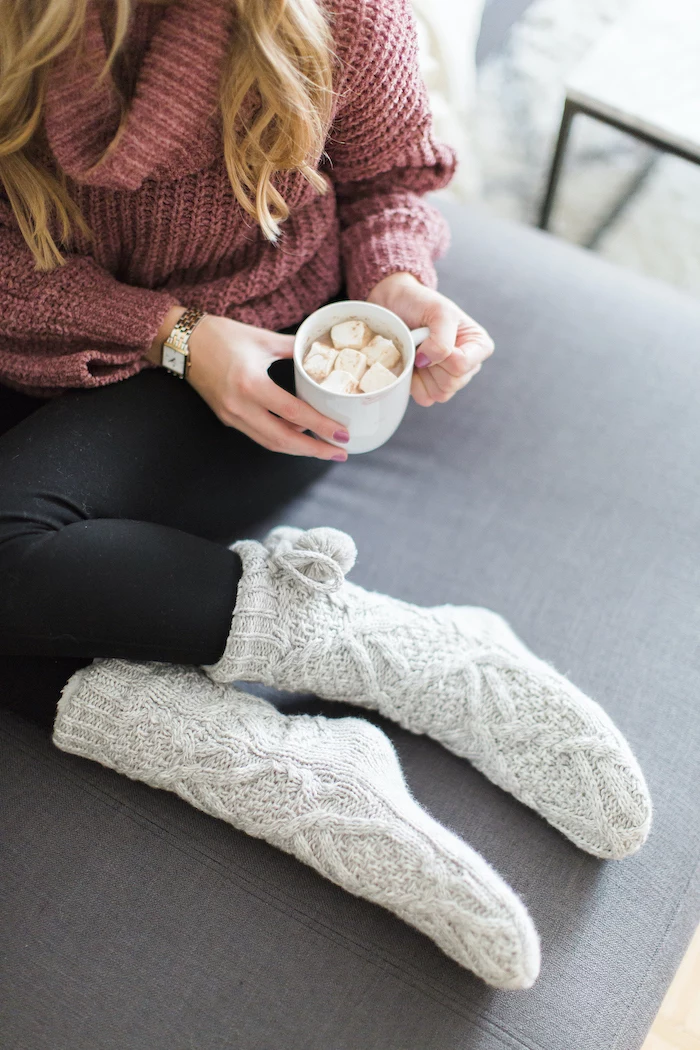 bonde woman wearing pink sweater and black tights, holding a cup with marshmallows, gifts for mom, grey knitted cozy socks