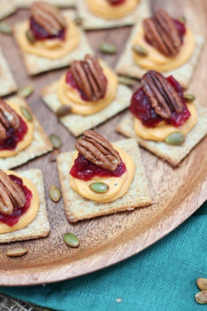 easy party snacks, crackers with sweet potato puree, cranberry sauce and walnuts, placed on wooden plate