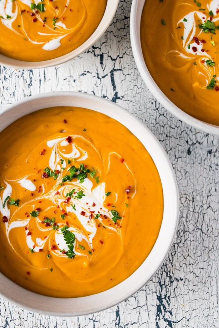 three bowls full of soup, fresh herbs on top for garnish, creamy chicken noodle soup, white wooden table