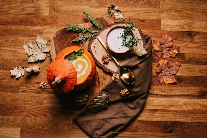 wooden table, fall arrangements on top, creamy chicken noodle soup, pumpkin soup, wooden board, brown table cloth, fall leaves