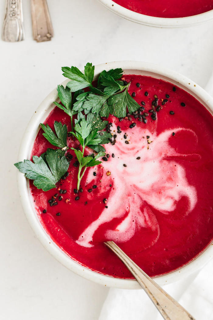 white ceramic bowl full of soup, chia seeds and fresh parsley for garnish, creamy chicken noodle soup, white table