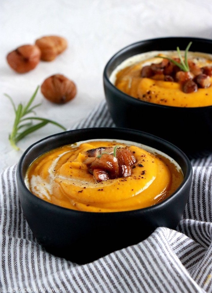 creamy chicken noodle soup, black ceramic bowls full of soup, nuts on top for garnish, grey and white striped table cloth