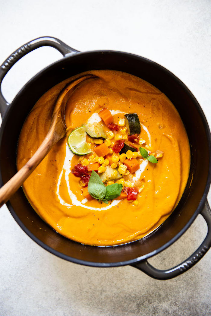 black pot full of soup, corn and carrots on top for garnish, wooden spoon inside, creamy chicken noodle soup