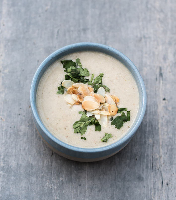 blue ceramic bowl full of soup, fresh parsley and slivered almonds on top, creamy potato soup recipe, wooden table