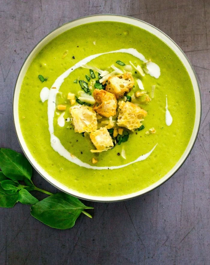 how to make soup, white bowl full of soup, croutons and fresh herbs on top, basil leaves on the side, grey countertop