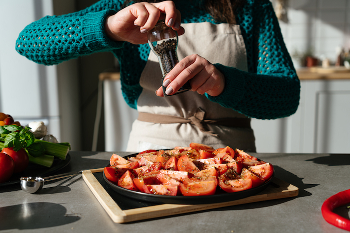 cut tomatoes arranged on black sheet pan, covered with black pepper, tomato soup, placed on wooden cutting board