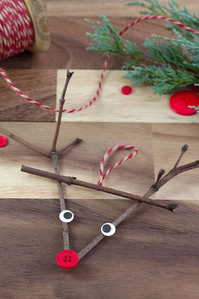 reindeer made of twigs, with googly eyes and red button for nose, preschool christmas crafts, placed on wooden surface