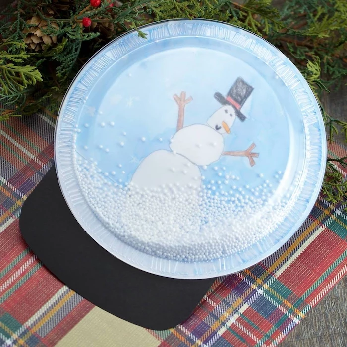 snow globe made of paper plate and plastic lid, faux snow inside, christmas ornament crafts, drawing of a snowman