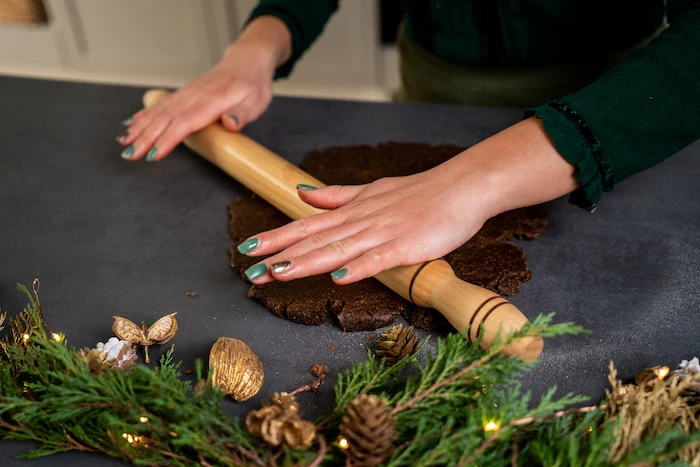 cookie dough being rolled out, spread on black surface, next to wreath with pinecones and lights, vegan gingerbread cookies