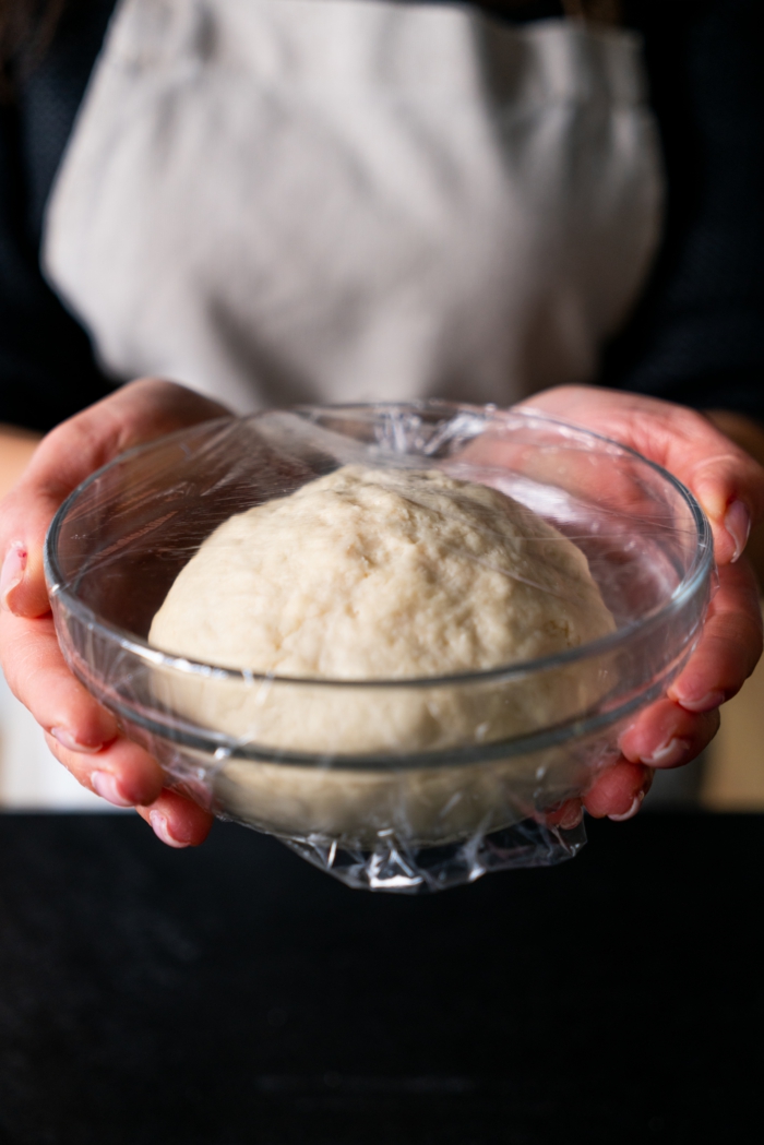 dough placed in glass bowl, naan bread, covered with plastic foil