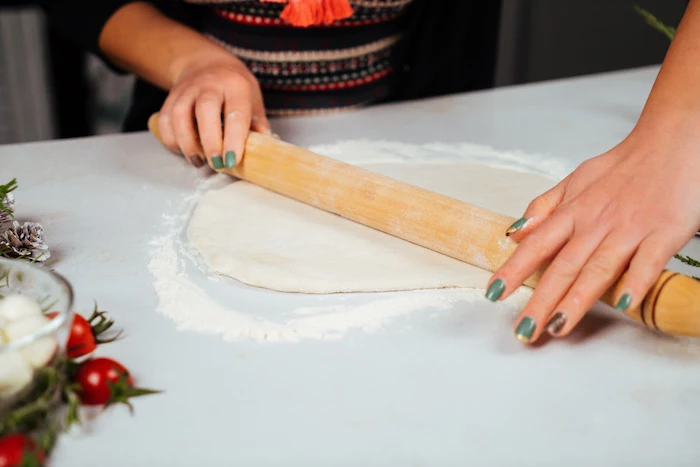 woman with green nail polish, rolling out dough on white surface, pull apart christmas bread, lightly floured surface